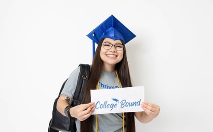 A student in a blue graduation cap and gown is smiling and holding a sign that says College Bound