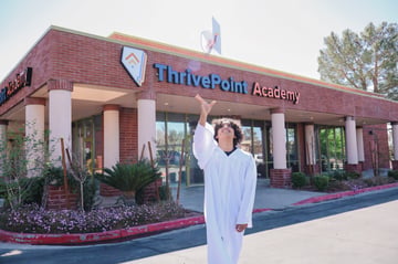 teen student in a white graduation gown throwing his cap in the air