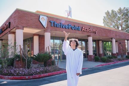 teen student wearing a white graduation gown throwing his cap in the air