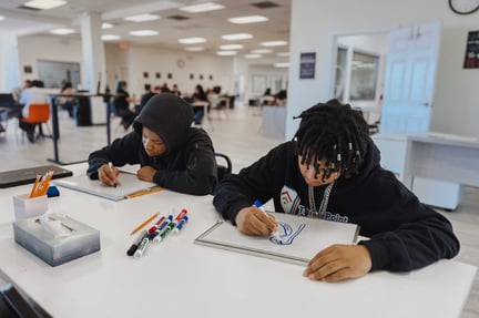 two teen students sitting at a desk writing on small whiteboards